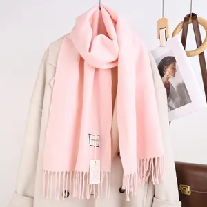 Nahaufnahme eines weichen rosa Wollmischschals mit Fransen und Stoffetiketten am Saum