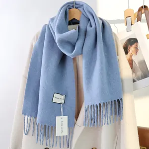 Detailansicht eines hellblauen Wollschals mit Fransen an einem Holzbügel