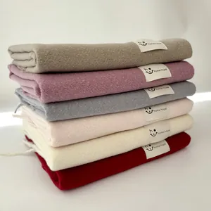 Dettaglio di sciarpe in cashmere impilate in vari colori con etichette tessute del marchio