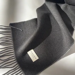 Dark grey wool muffler with classic long tassels and soft folded texture on white background