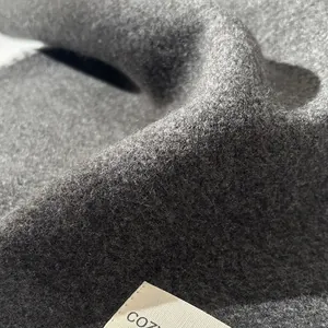 Macro shot of dark grey wool fabric with a soft fiber texture and 'COZY' brand label
