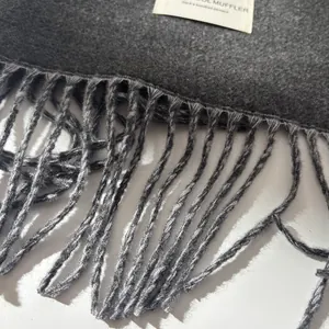 Close-up of dark grey wool muffler texture with tassel detail and woven label
