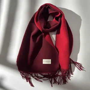 Detail of red wool muffler with fringe and woven label on thick textured fabric