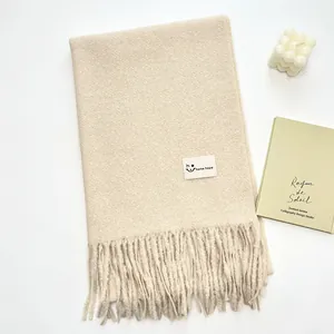 Dettaglio di sciarpa beige effetto cashmere con frange e etichetta minimalista