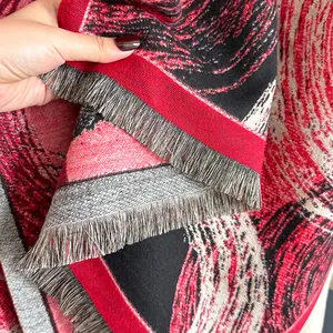 Detail of a thick woven shawl featuring red, black, and beige abstract fluid patterns with fringe