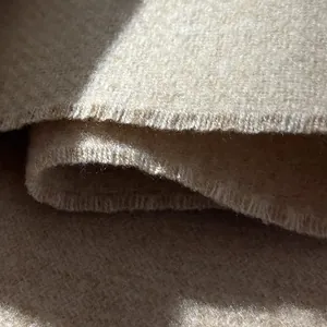 Macro detail showing thick beige wool fabric texture and reinforced hem stitching