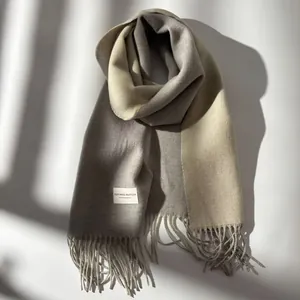 Detailed close-up of thick wool scarf with fringe and a woven label on neutral surface