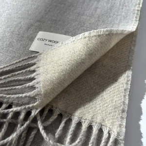Detail of double-sided grey and cream wool scarf with soft tassels and woven logo label