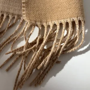 Close-up of soft camel wool scarf fabric with elegant tassel details and textured weave