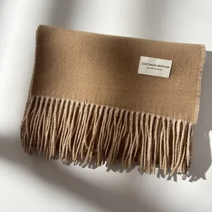 Close-up of camel wool scarf featuring soft fringe edges and a minimalist square fabric label