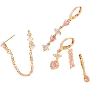 Dettaglio di orecchini dorati con zirconi rosa e ciondoli a cuore bianco in set