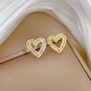 Close-up of golden heart earrings with sparkling rectangular zircon stones on silk