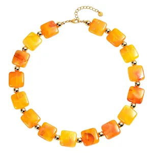 Primo piano di vivaci perle quadrate in resina arancione e accenti dorati su una collana