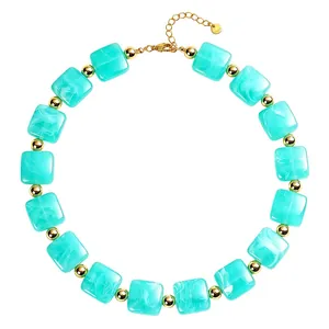 Dettaglio ravvicinato di collana con perle di resina turchese e sfere dorate lucide.