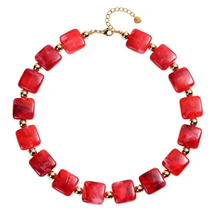 Primo piano di una collana con perle di resina quadrate marmorizzate rosse e dettagli oro