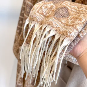Dettaglio della trama jacquard e delle nappe bianche su una sciarpa a quadri spessa