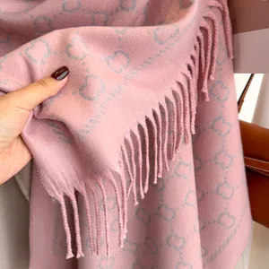 Gros plan sur l'écharpe rose tricotée avec motifs de cœurs gris et détails de franges