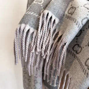 Gros plan détaillé d'une écharpe grise à monogramme avec franges et texture douce