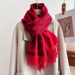 Détail d'une écharpe en maille rouge avec motifs de lettres et franges sur un manteau beige