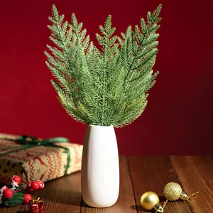 Norfolk pine branches in white ceramic vase on a festive table with red background