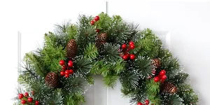 Detail of a Christmas wreath with pine needles, red berries, cones and snow effect