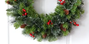 Close-up of Christmas wreath with pine needles, cones, and red berries on a white door