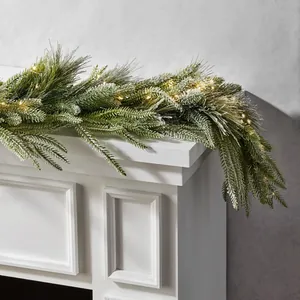 Kunstmatige kerstslinger met warme LED-verlichting en sneeuwvlokken op een witte open haard