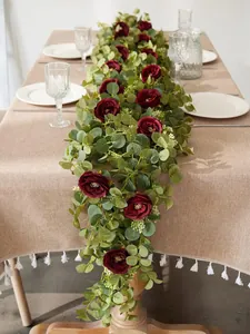 Detalle de guirnalda de rosas burdeos y eucalipto sobre mantel con flecos decorativo
