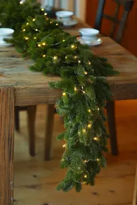 Macro shot of artificial pine needle garland featuring warm white LED fairy lights on wood