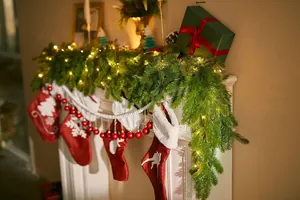 Close-up of lit Christmas garland with warm LED lights and red ornaments on mantel