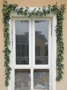 Close-up of lifelike green pine needle garland with warm LED fairy lights on a window