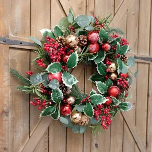 Klassischer Weihnachtskranz mit roten Beeren, Zapfen und Goldkugeln an einer rustikalen Holztür