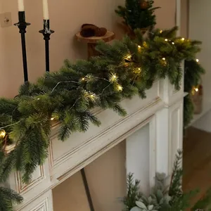 Detail of green artificial pine garland with warm LED lights on a white mantelpiece