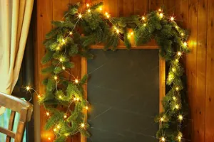 Close-up of dense green Christmas pine garland with warm white LED starry lights on a wall
