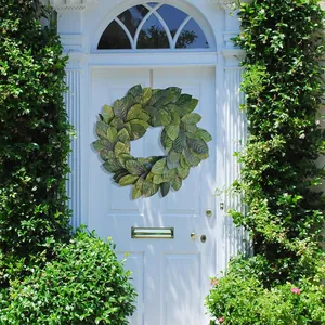 Lush evergreen artificial magnolia leaf wreath hanging on a white wooden front door