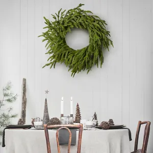 Green faux cedar Christmas wreath hanging on a white wooden wall in a cozy home setting