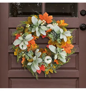 Detailed view of autumn wreath with maple leaves and white pumpkins on a dark wood door
