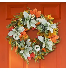 Detailed close-up of autumn wreath with white pumpkins, maple leaves on an orange wooden door
