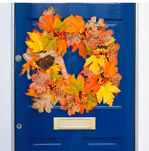 Close-up of fall wreath with maple leaves, red berries, and burlap bow on a blue door