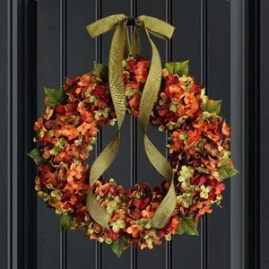 Herfstkrans voor de deur met levendige oranje en rode kunsthortensia's en groen lint