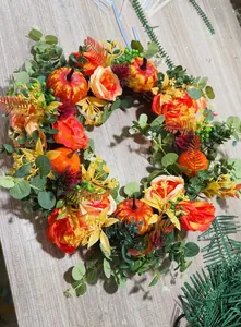 Detailed view of autumn wreath with orange pumpkins, roses and eucalyptus on wood