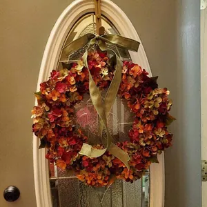Herfstkrans van hydrangea met oranje bloemen en groen satijnen lint voor de voordeur