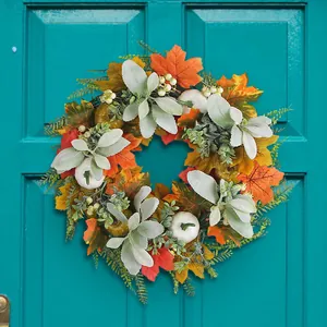 Autumn wreath with orange maple leaves and white pumpkins hanging on a green wooden door