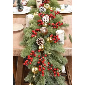 Holiday garland with green pine needles, red berries, and gold balls on wooden table