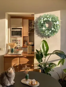 Detail eines künstlichen Eukalyptus-Kranzes mit weißen Blüten in warmer Wohnumgebung