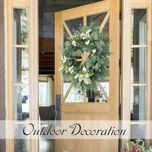 Detail eines Eukalyptuskranzes mit Lilien und Gänseblümchen an einer Holztür aus Glas