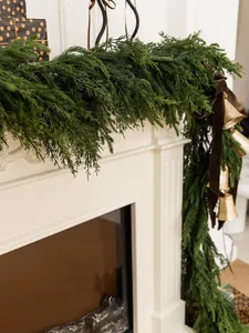 Close-up of artificial Norfolk Pine garland with brass bells and brown velvet bow on mantel