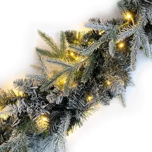 Close-up of snow-flocked pine garland with warm LED lights on white background