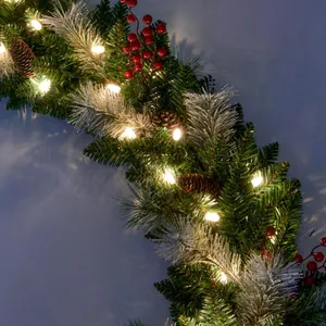 Detailed close-up of Christmas garland with pine cones, red berries and warm LED lights