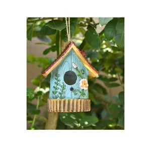 Detail of blue resin birdhouse with red roof and flowers hanging from a garden tree